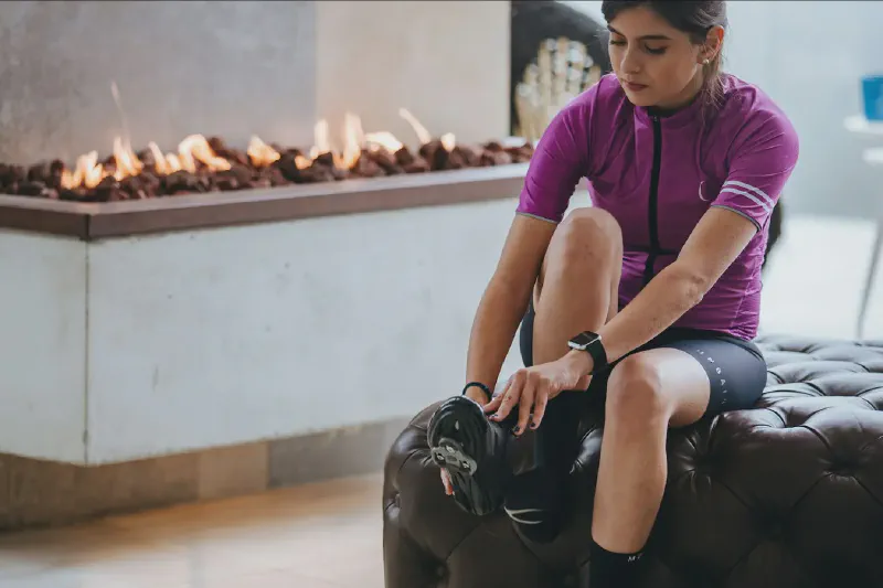 A compact upright exercise bike positioned in a small apartment living room beside a folded exercise mat