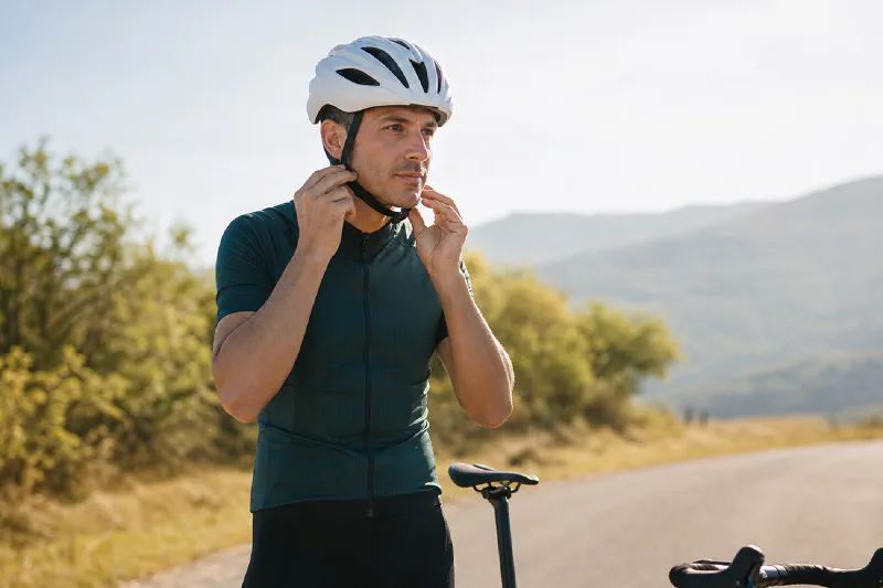 A recreational road cyclist adjusting the chin straps of an unbranded helmet